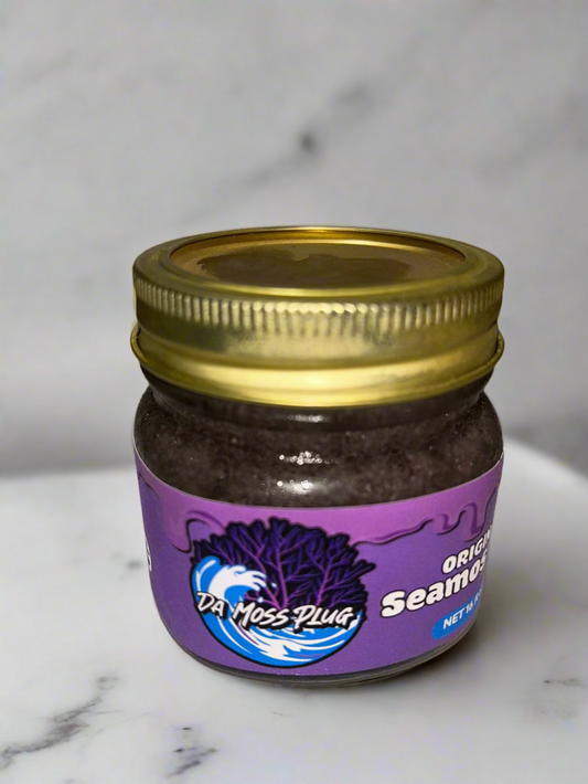 Small glass jar of Da Moss Plug Original Sea Moss Gel with a gold lid and purple label, placed on a white marble surface with a gray background.